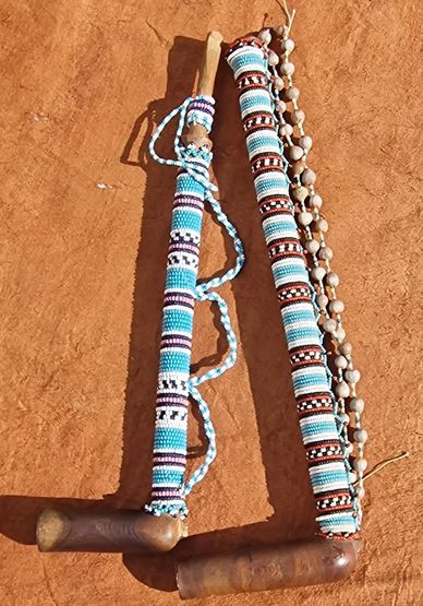 Two traditional beaded wooden clubs on reddish ground.