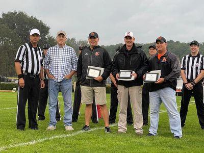 Six men standing on a football field, three holding plaques.