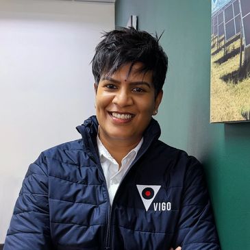Smiling person wearing a Vigo jacket, standing against a green wall.