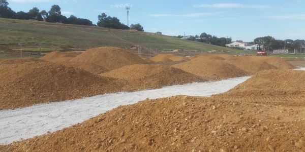 Several dirt mounds on a construction site with a gravel path.