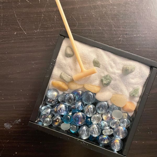Sand tray with shiny blue pebbles in sand  with sand tray rake on psychotherapist’s office desk.