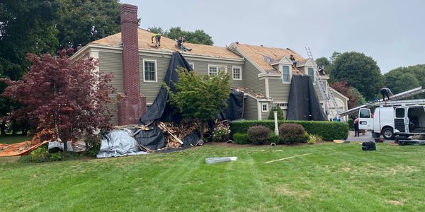 Workers are replacing the roof of a large suburban house on an overcast day.