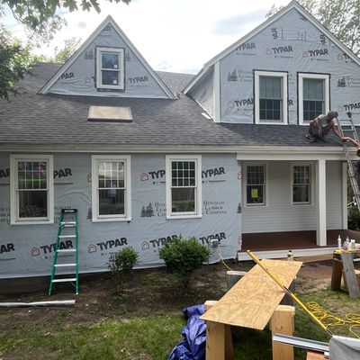 Workers renovating a house exterior with ladders and construction materials present.