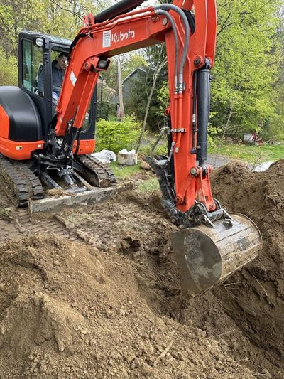 A small excavator digging into the dirt at a construction site, with soil being displaced by its buc