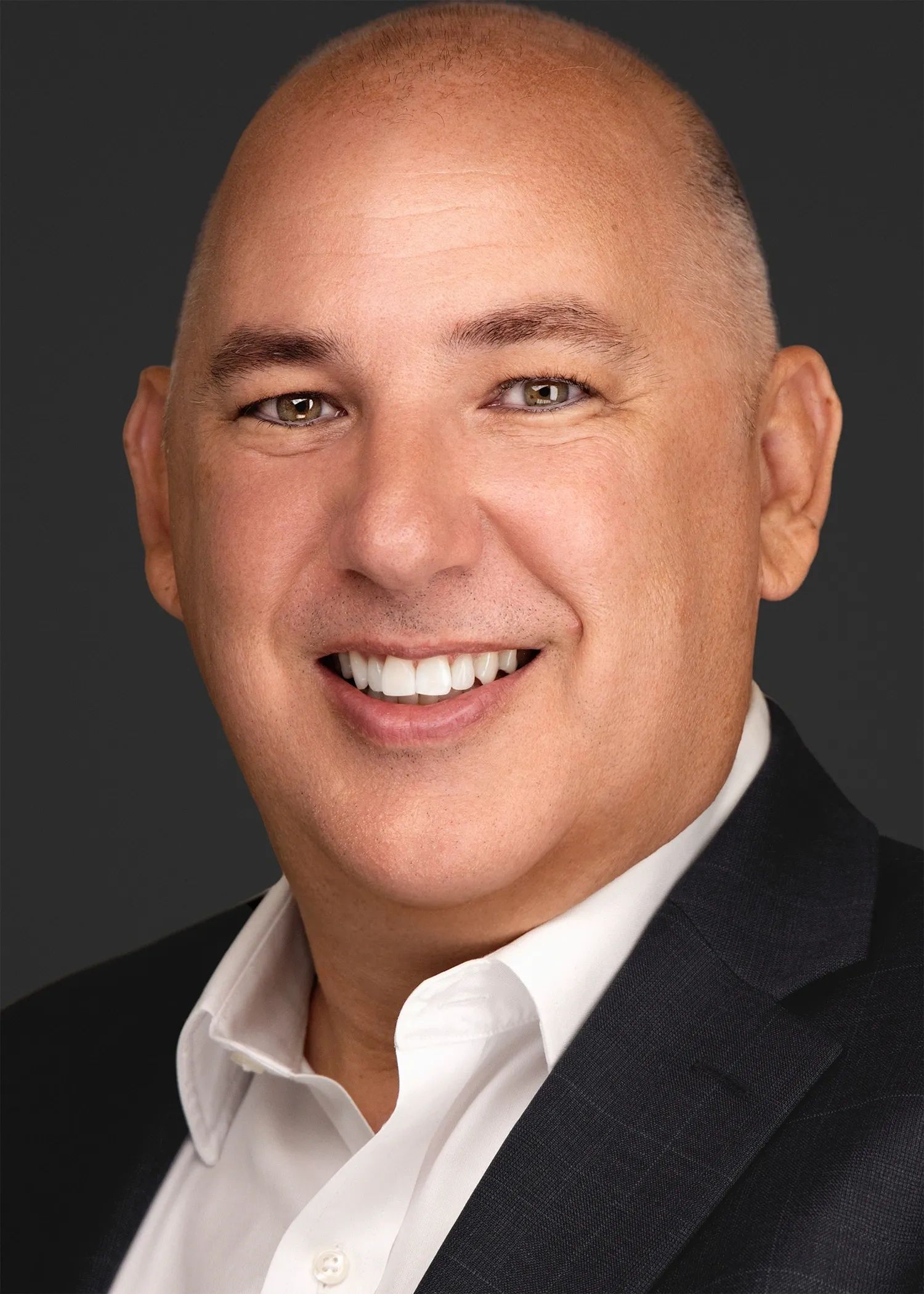 Smiling bald man in business attire with a dark background.