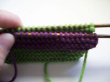 Two knitting needles with the decorative stitches placed in front of the working body of yarn.