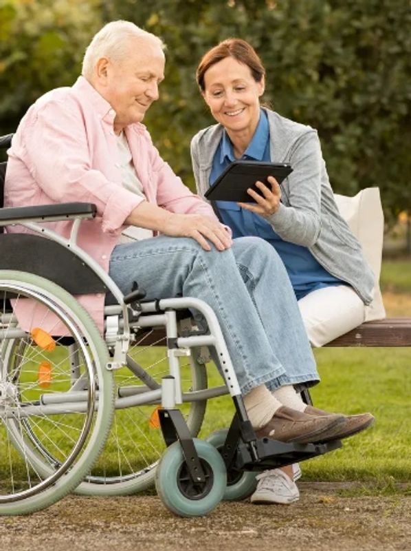 Woman shows tablet to elderly man in wheelchair.