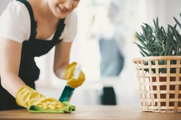 Woman cleaning a wooden surface wearing yellow gloves and holding a spray bottle.