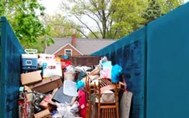 A large dumpster filled with various discarded household items outdoors.
