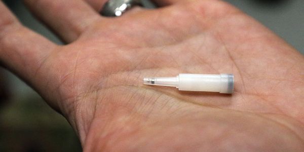 Small white medical device or component held in a person's palm.