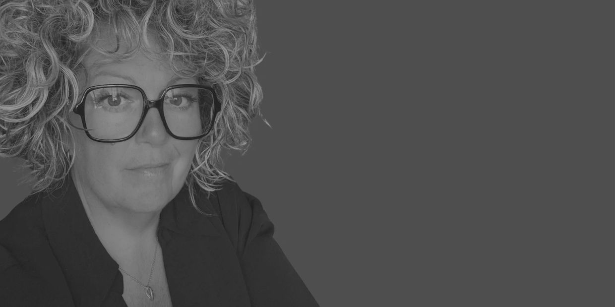 Femme aux cheveux bouclés et lunettes, regardant la caméra.