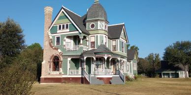 A large 3 story Victorian home with ornate trim and a large curved chimney.