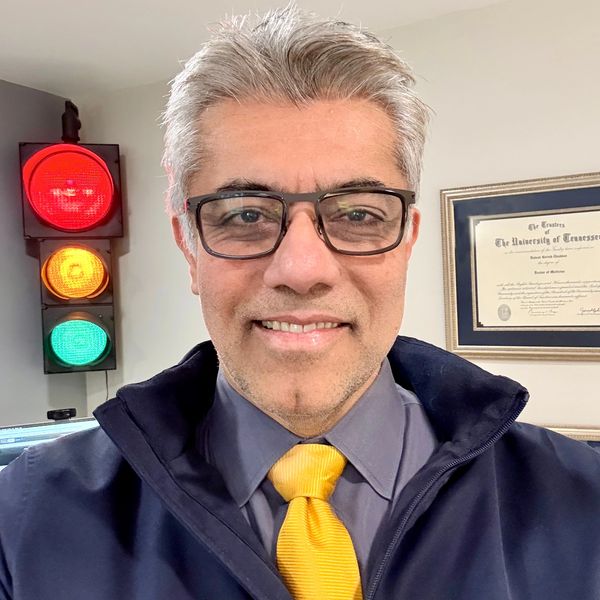 Smiling man wearing glasses, yellow tie, and dark jacket indoors.