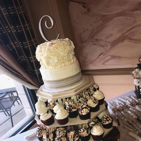 Elegant two-tier cake with floral design and cupcakes on a multi-level stand.