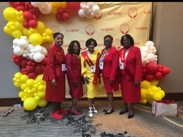 Five women dressed in red and yellow smiling at a NANBPWC event with colorful balloon decorations.