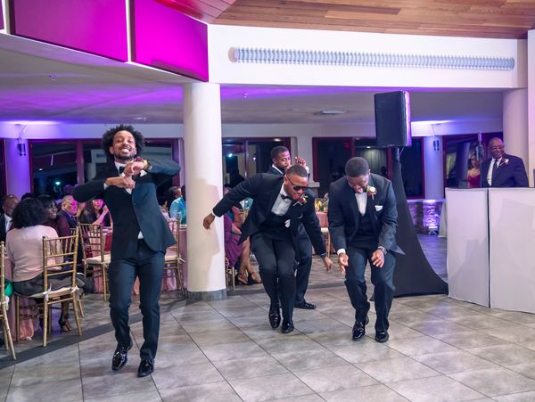 Four men in suits dancing at an indoor event.