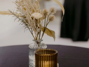 Dried floral arrangement in a clear vase with amber glass on a black tablecloth.