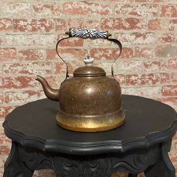 Vintage brass kettle with decorative handle on ornate black table.