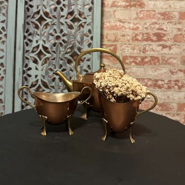 Vintage brass tea set with dried flowers on a black table.