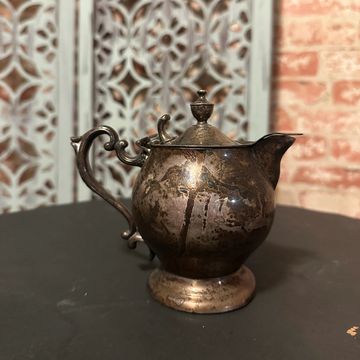 Antique tarnished silver teapot on a dark surface.