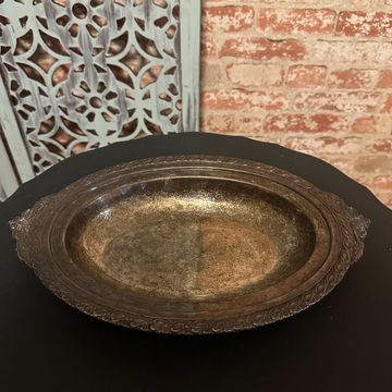 Ornate antique metal serving dish on a black table with a decorative backdrop.