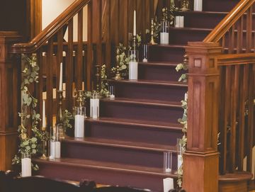 Elegant wooden staircase decorated with candles and greenery in a warmly lit event space.