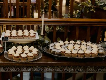Assorted cupcakes displayed on trays with a stack of white plates beside them.
