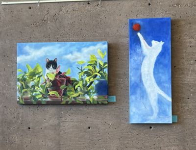 Two paintings of cats, one sitting among plants and the other reaching for a ball.