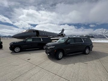 Two black SUVs parked near a private jet on a cloudy day.
