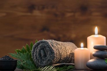 Rolled towel, candles, and spa stones arranged for relaxation.