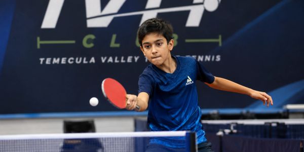 Young boy playing table tennis, focused on hitting the ball.