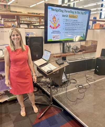 A woman in a red dress stands next to a presentation screen about digital parenting.