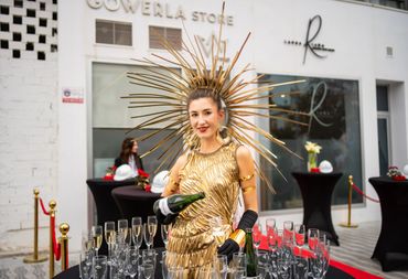 Woman dressed in gold pouring champagne at an outdoor event.