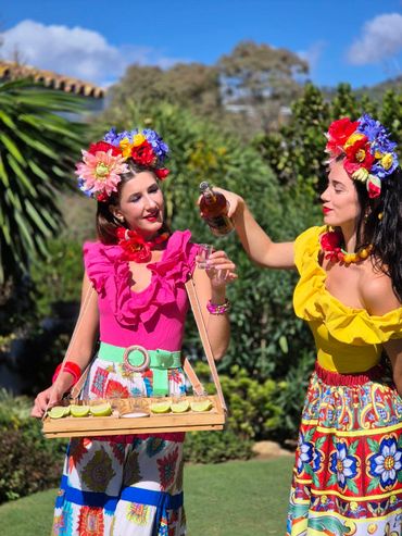 Two women in vibrant floral outfits sharing drinks outdoors.