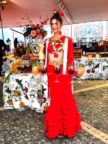 Woman in vibrant red flamenco dress serving colorful drinks at an elegant event.