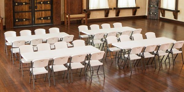 Empty white folding chairs and tables arranged in a wooden room.
