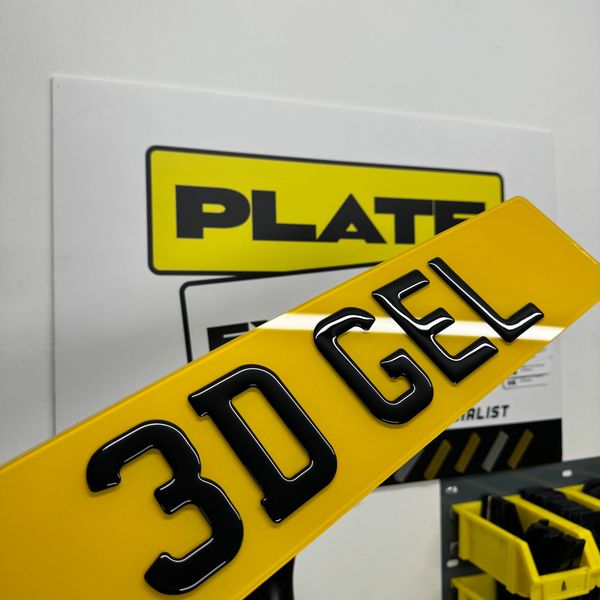 A yellow 3D gel license plate with black letters in a workshop setting.