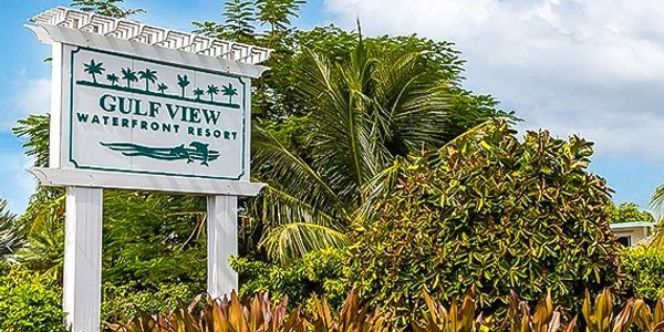 Sign for Gulf View Waterfront Resort surrounded by tropical plants under a bright sky.