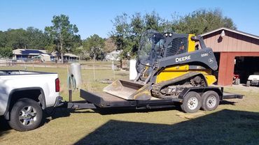 A yellow John Deere 333G skid steer on a trailer hitched to a white pickup truck.