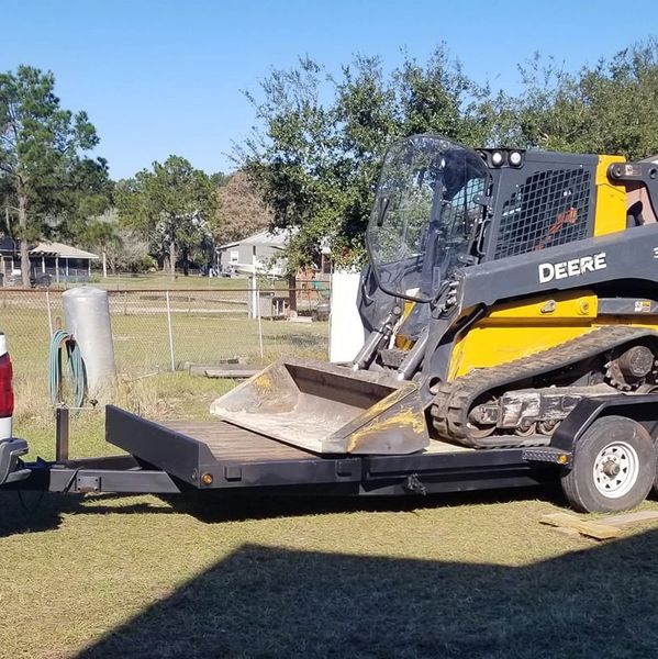 A yellow John Deere 333G skid steer on a trailer hitched to a white pickup truck.