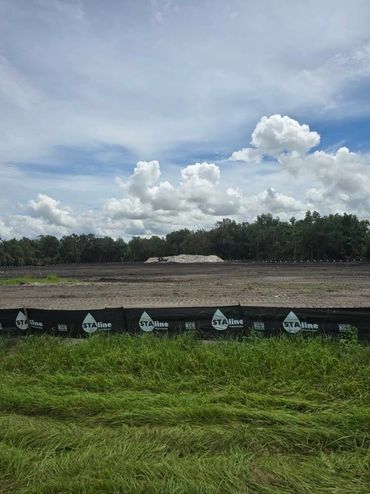 A cleared field with construction barriers under a cloudy sky.