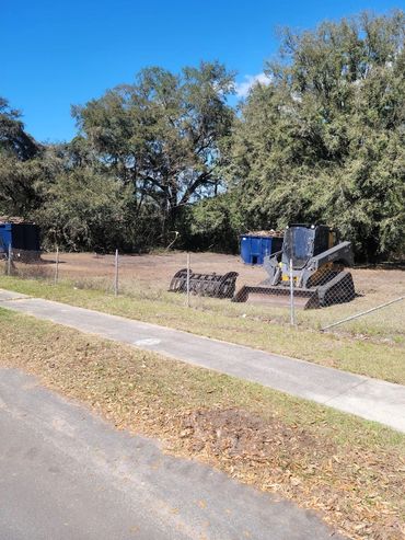 A Deere construction vehicle parked behind a chain-link fence on a sunny day.