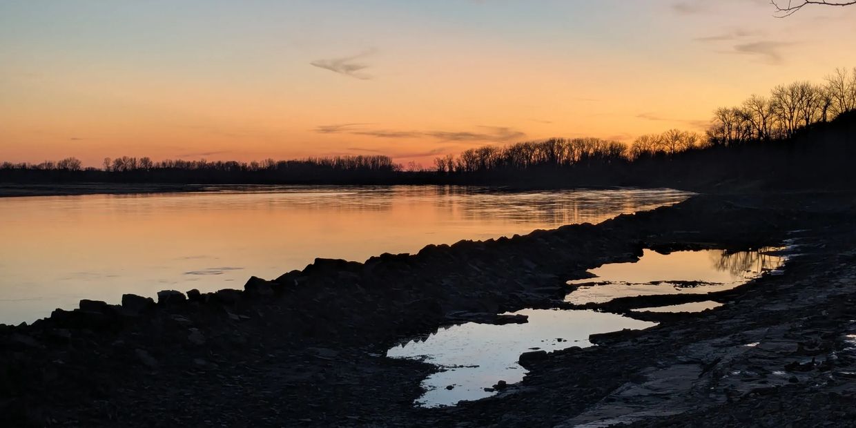 Tranquil river at sunset with silhouetted trees and reflective water pools.