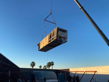 A large industrial unit being lifted by a crane on a clear day.