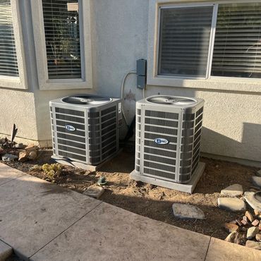 Two AC Pro air conditioning units outside a house with a stone and dirt landscape.