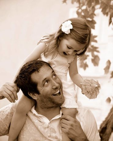 Adorable duotone image of father looking upwards towards his young daughter on his shoulders.