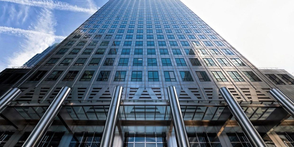 Upward view of a modern glass skyscraper with metallic pillars.