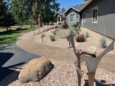 Modern gray house with stone garden and metal sculpture in front yard.