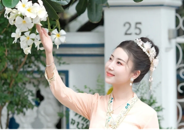 A woman in traditional attire admires white flowers outdoors.