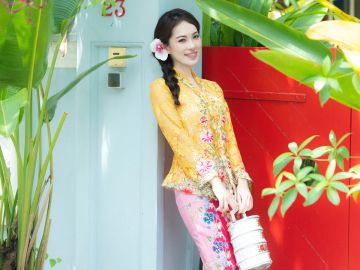 Woman in traditional dress holding container with flower in hair.